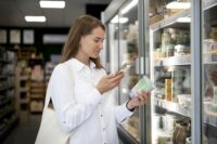Devojka skenira QR kod na proizvodu svojim pametnim telefonom u supermarketu.