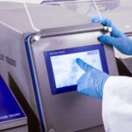 Ekran Mettler Toledo metal detektora i ruka operatera koja pririska opcijua na touch screen ekranu.